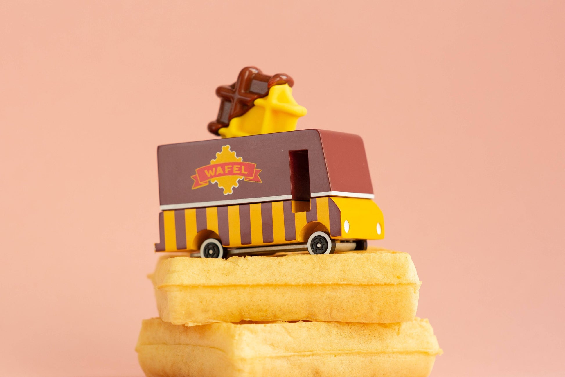 Toy ice cream truck on a stack of waffles with a pink background